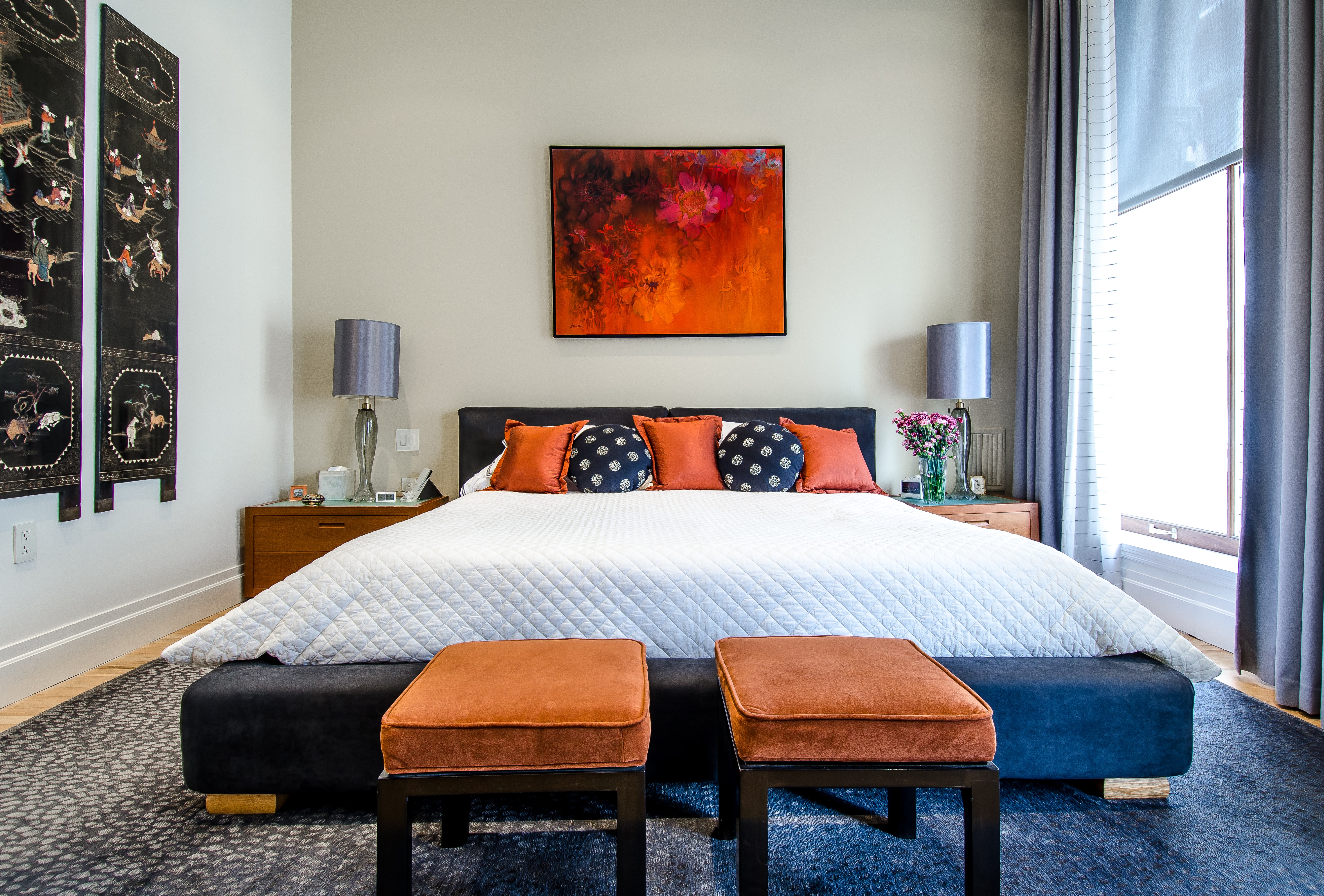 The master bedroom with light shining through a large side window onto a white king sized bed with accents in orange.